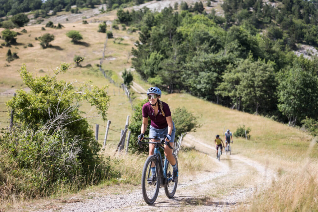 Veduta dall'alto di un tornante su strada bianca dove un gruppo di ciclisti affronta una curva immerso nel verde intenso delle Foreste Casentinesi durante la tappa di Santa Sofia.