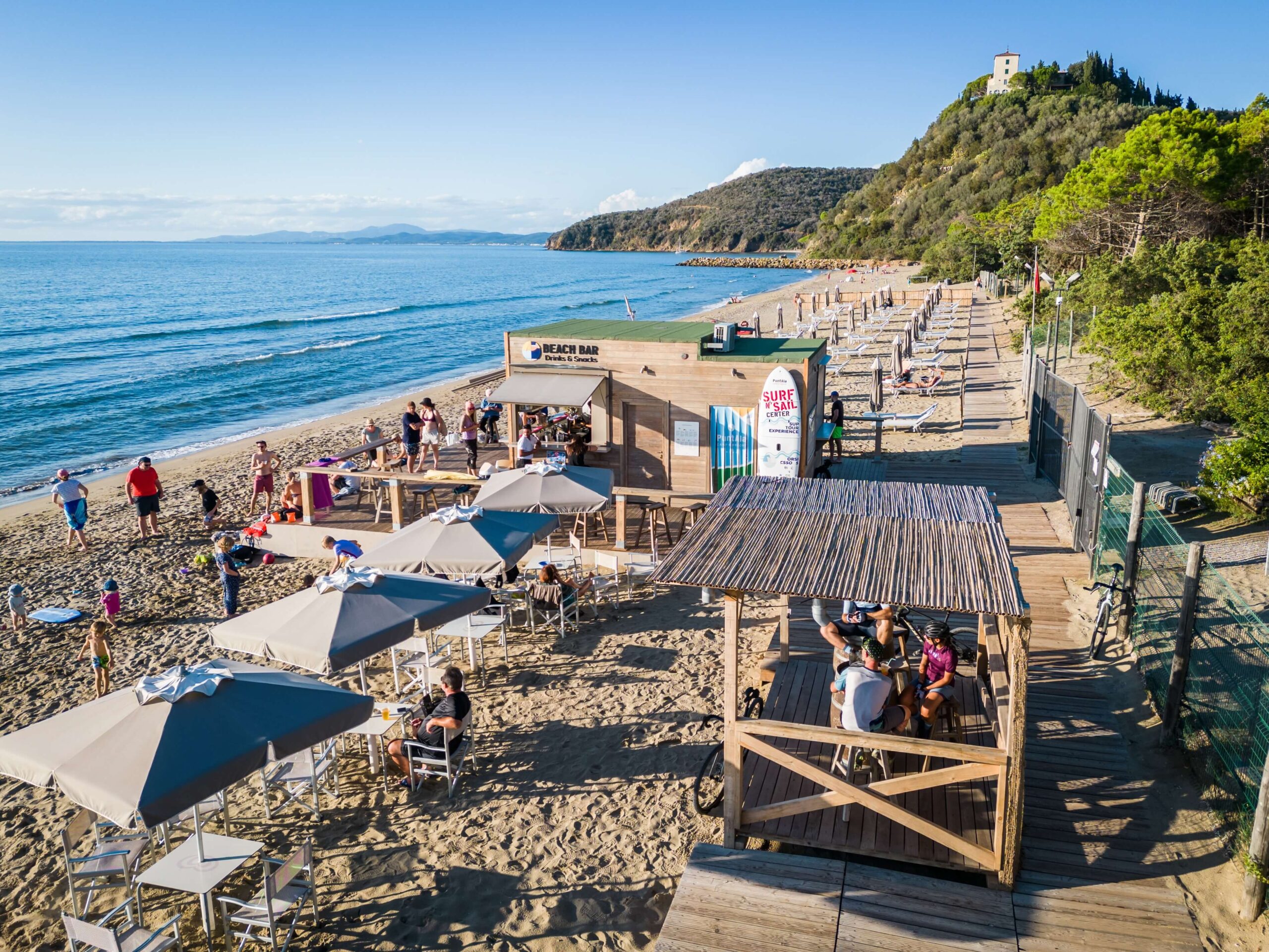 Beach bar sulla spiaggia di Punta Ala con ciclisti e persone che si rilassano dopo il percorso gravel durante l’evento Unpaved Roads in Toscana
