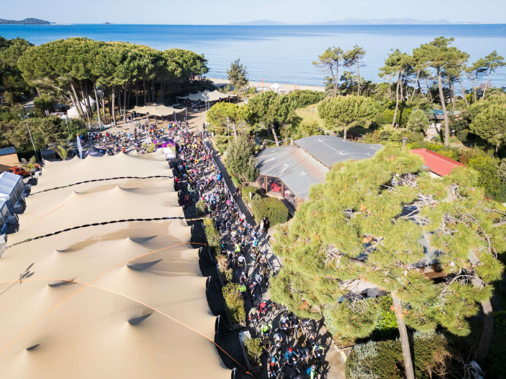 Vista aerea dell’evento gravel Unpaved Roads a Punta Ala con village, partecipanti e mare sullo sfondo