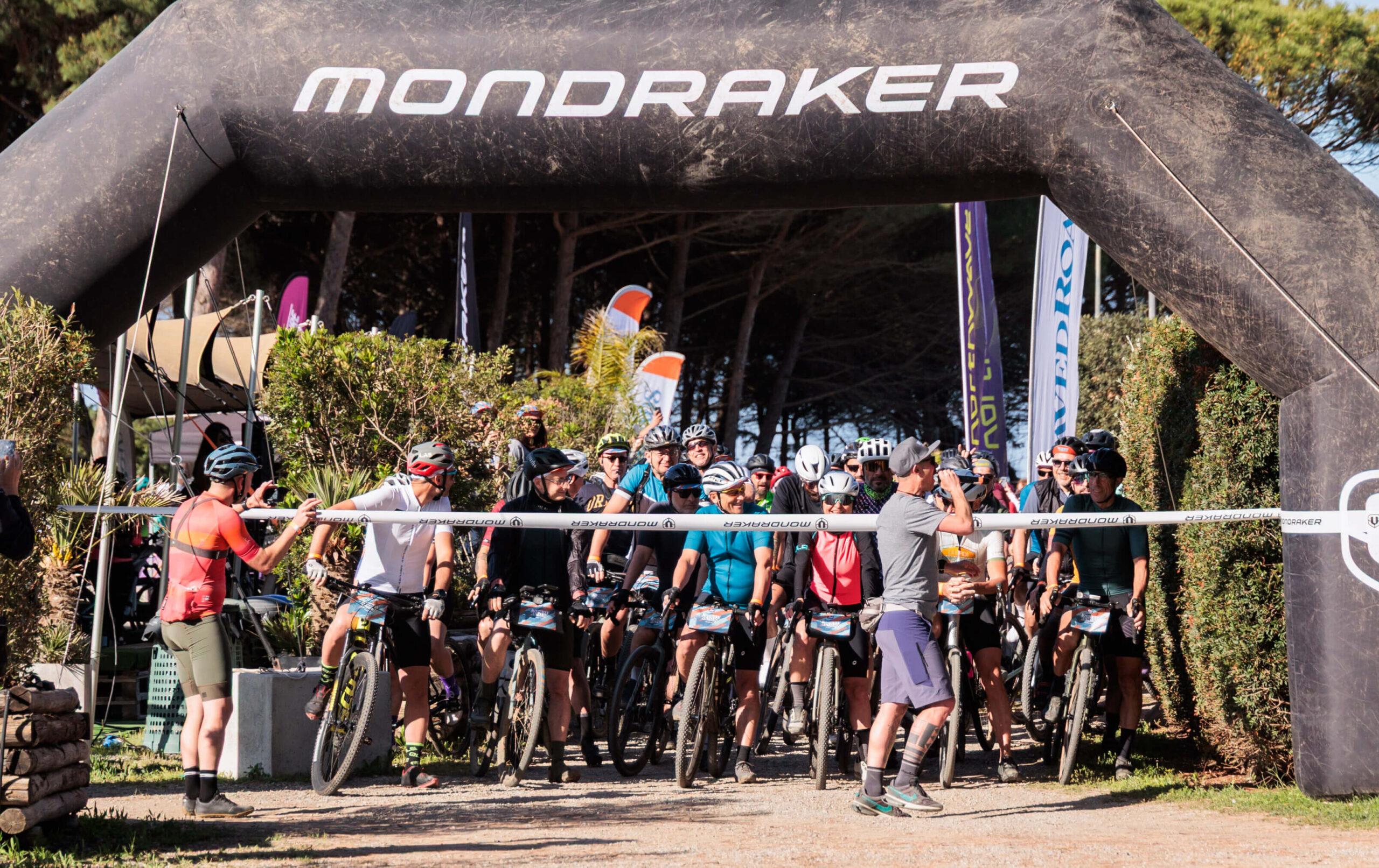 Ciclisti alla linea di partenza dell’evento gravel Unpaved Roads a Punta Ala sotto l’arco Mondraker