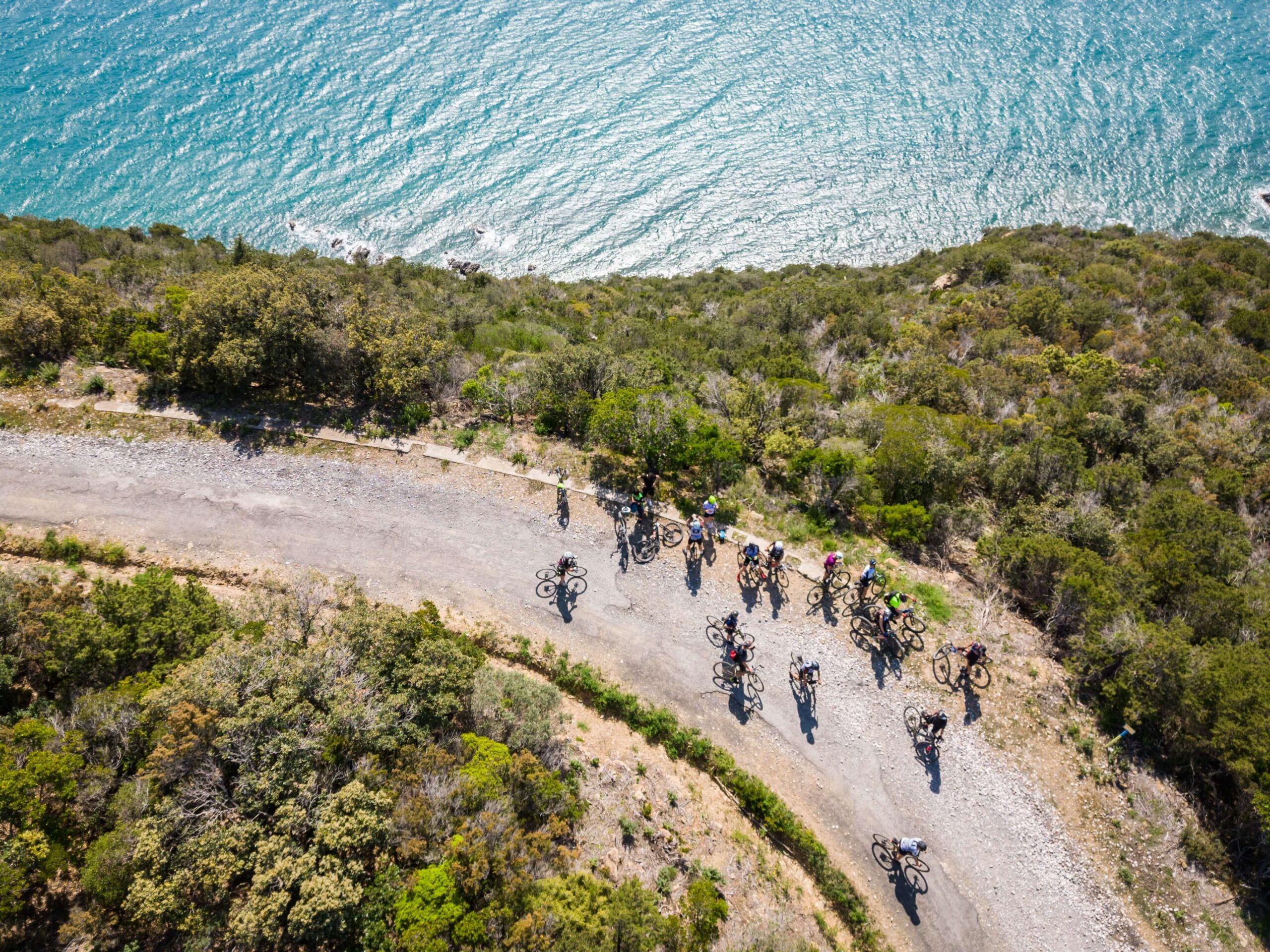 Gruppo di ciclisti su percorso gravel panoramico a strapiombo sul mare durante l’evento Unpaved Roads a Punta Ala in Toscana