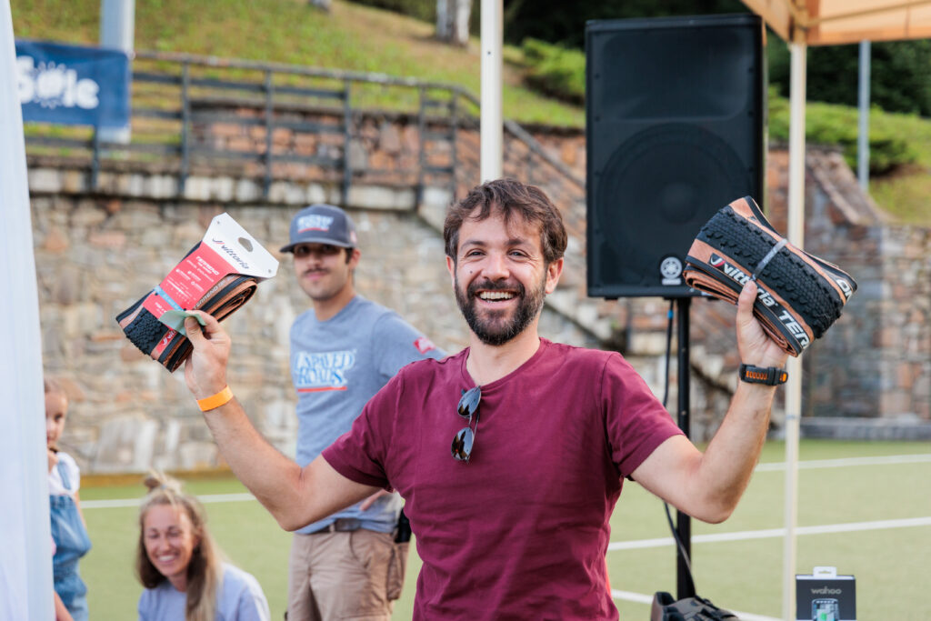 Un partecipante felice tiene in mano due copertoni Vittoria Terreno come premio durante la cerimonia di premiazione dell'evento Unpaved Roads in Val di Sole.