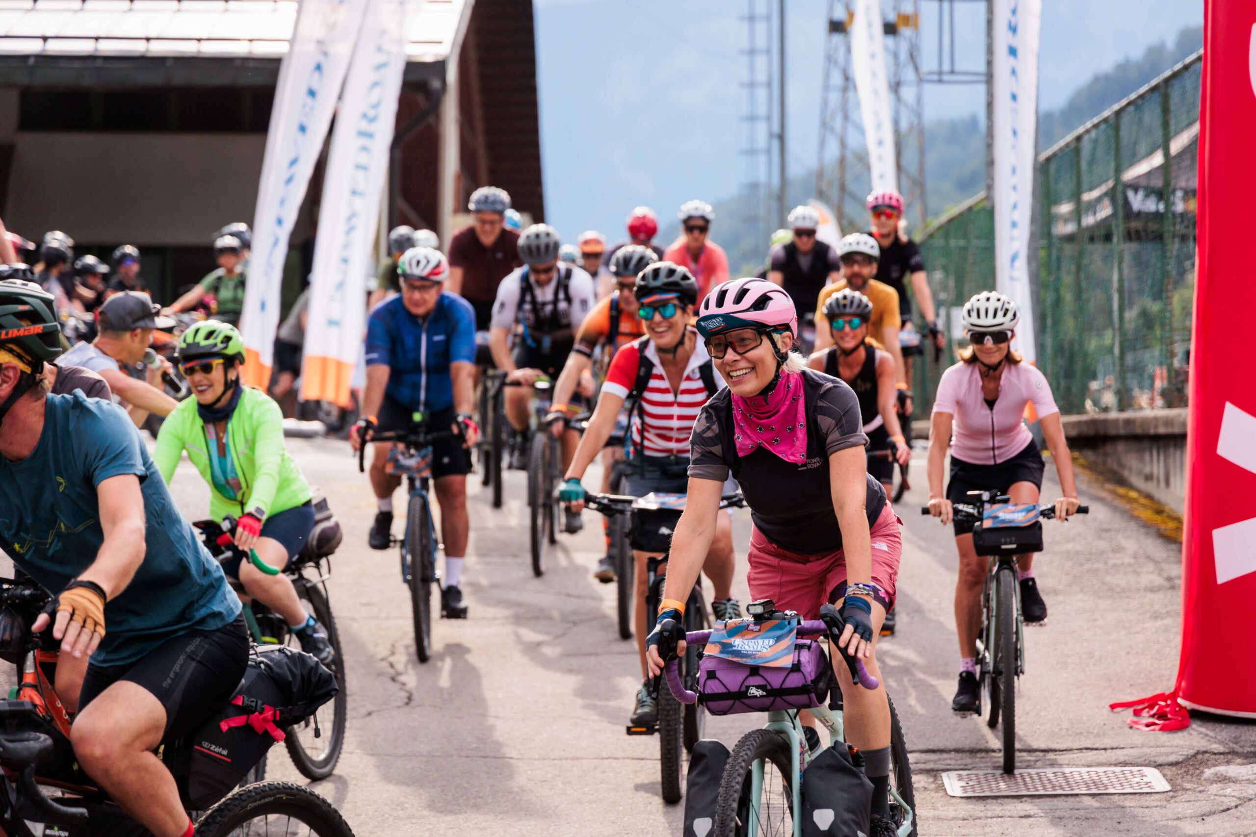 Il gruppo di ciclisti schierato sulla linea di partenza dell'evento gravel Unpaved Roads in Val di Sole, pronti al via tra i totem rossi.