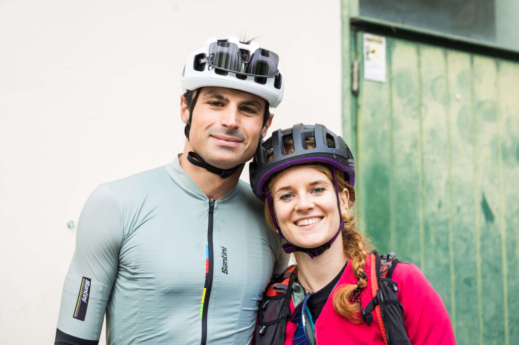 Ritratto di due ciclisti sorridenti con casco durante l’evento Unpaved Roads, simbolo dello spirito community gravel.