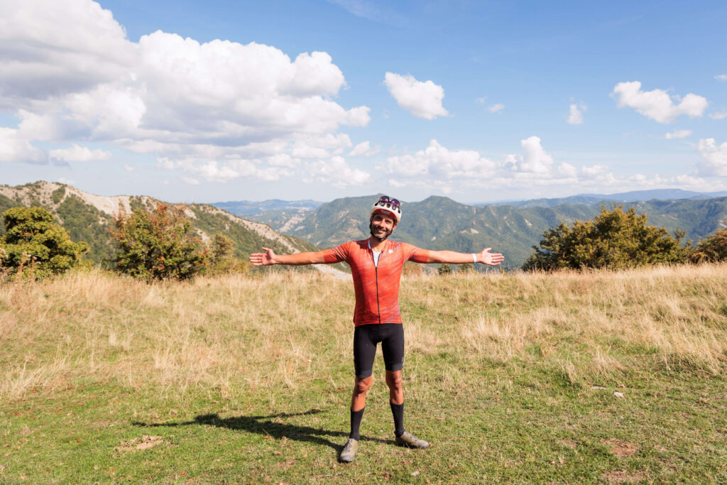Ciclista sorridente con le braccia aperte davanti al panorama montano delle Foreste Casentinesi durante Unpaved Roads.